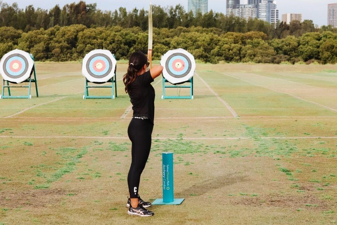 woman practicing archery, aiming her bow and arrow at a target
